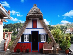 A traditional house with a thatched roof, a red door, and a white and blue facade. - O Colmo (Santana)
