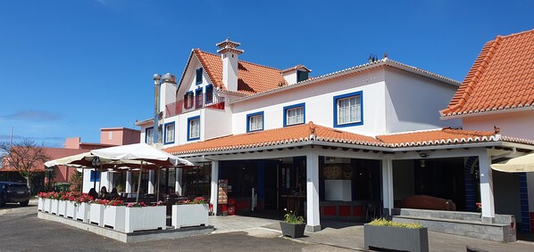 A two-story building with a tiled roof, a balcony, and outdoor seating with umbrellas.