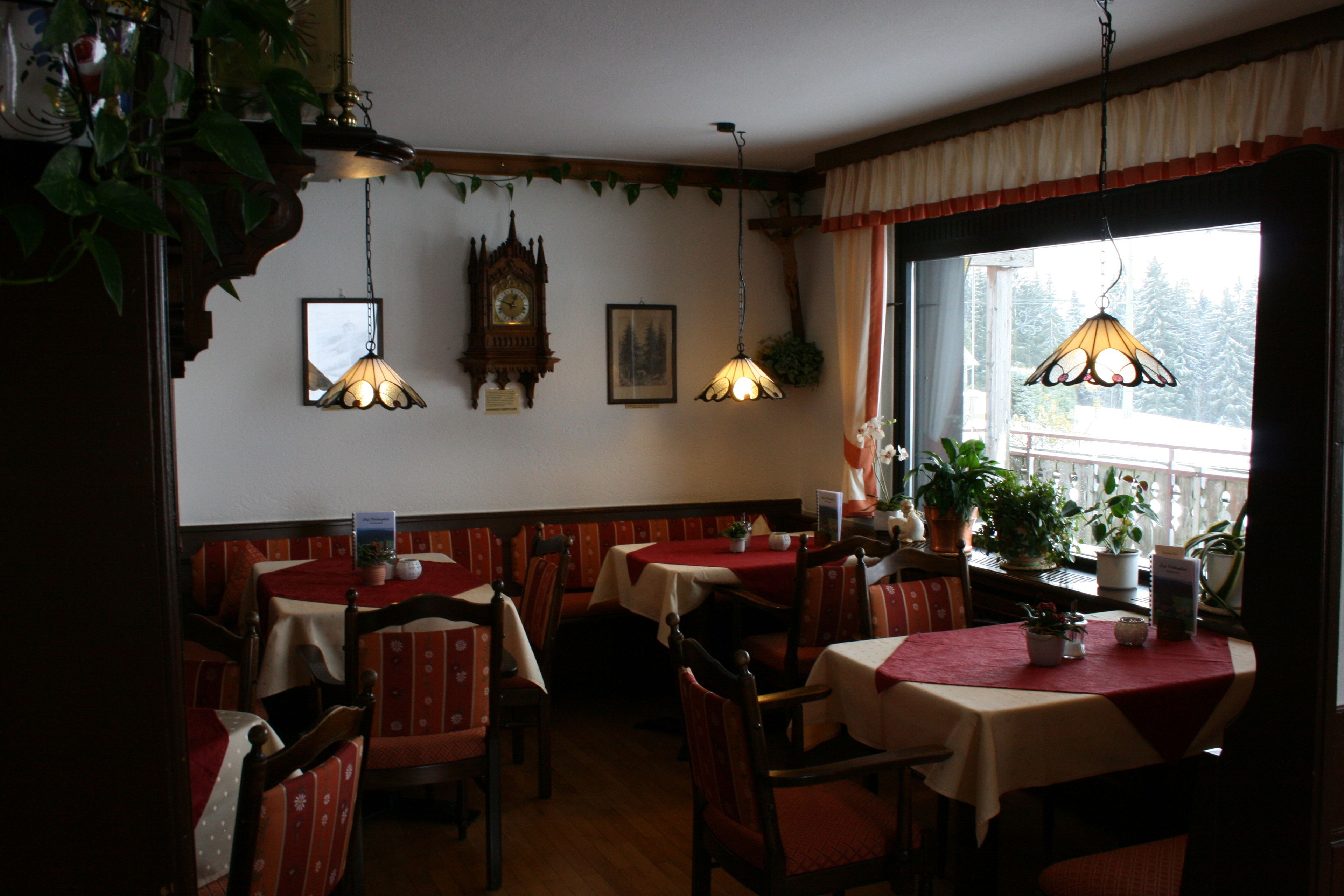 A dining area with tables and chairs, a clock on the wall, and hanging lamps.