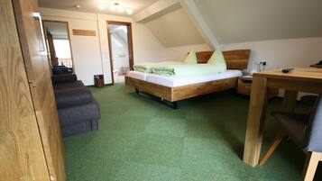 A bedroom with a wooden bed, a desk, and a chair. There is a bathroom visible through an open door.