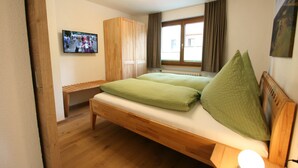 Ein Schlafzimmer mit einem hölzernen Bett, einer Bank, einem Kleiderschrank und einem Fernseher an der Wand.