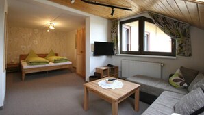 Ein gemütliches Wohnzimmer mit Holzbalkendecke, einer Couch, einem kleinen Tisch und einem Fernseher.