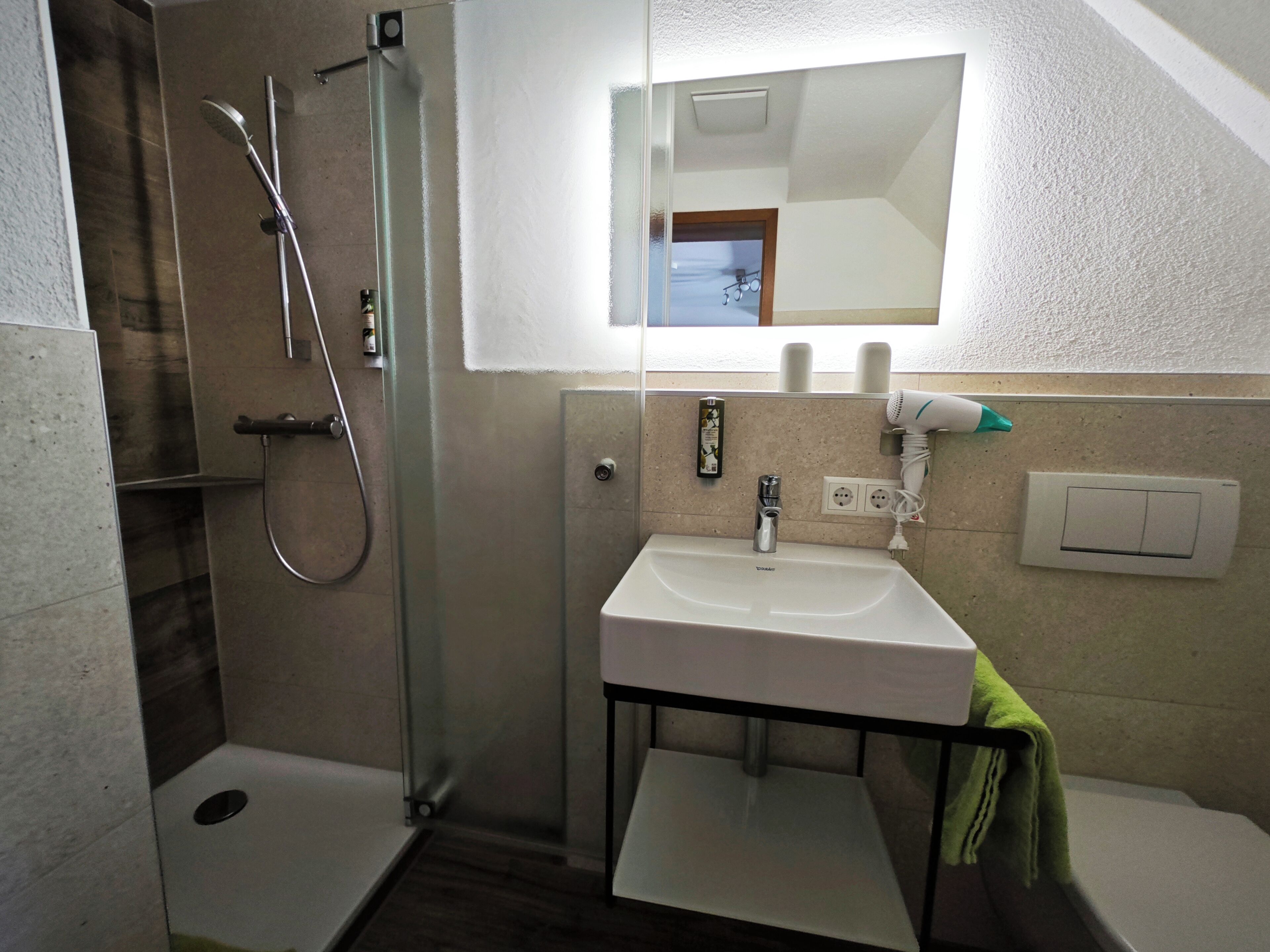 Un baño con cabina de ducha de vidrio, un lavabo blanco y un espejo encima.