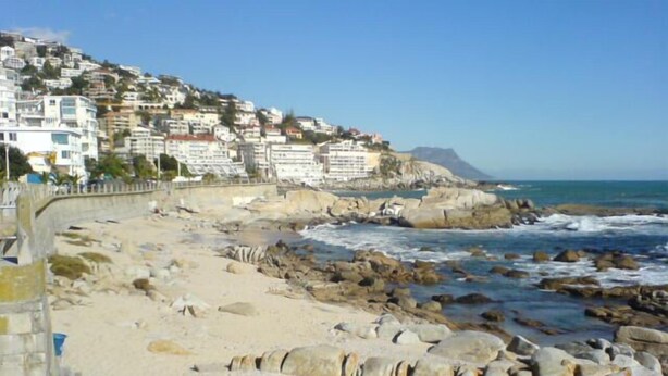 Un hôtel situé sur la côte, avec une plage rocheuse, un mur de pierre et des bâtiments construits sur une colline.