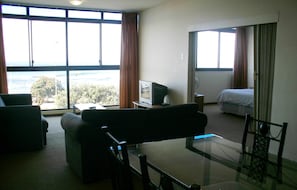 A hotel room with a large window, a bed, a desk with a computer, and a chair. - Mouille Grange 203 - Apartment (Cape Town)