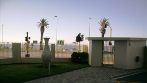 Una entrada con portón, una palmera, un semáforo y una señal de tráfico al fondo.