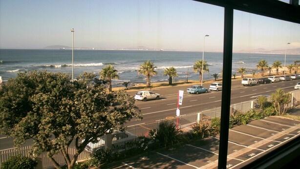 Vista del océano con palmeras y coches aparcados a lo largo de la playa.