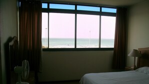 Habitación de hotel con un ventanal grande que ofrece vistas a la playa y al océano.