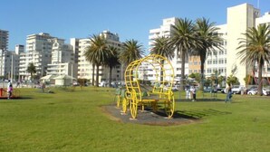 A park with a yellow sculpture, palm trees, and modern buildings in the background. - Glenlodge 401 - Apartment (Cape Town)