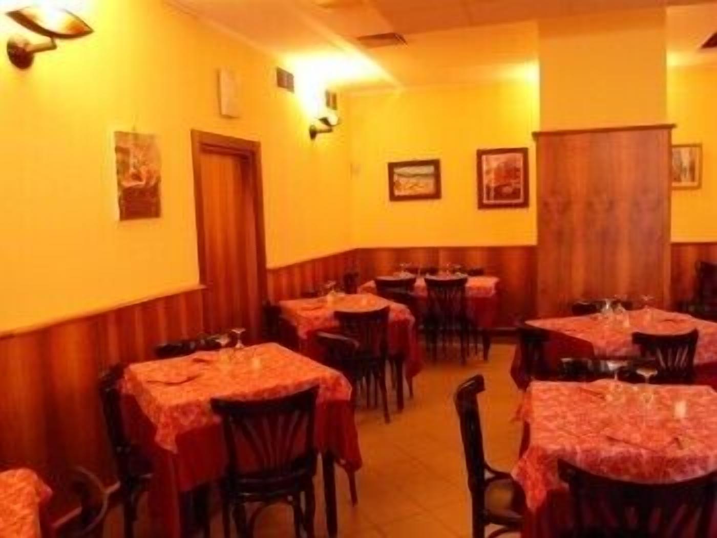 A restaurant with multiple tables and chairs, wooden paneling on the walls, and framed pictures on the walls.