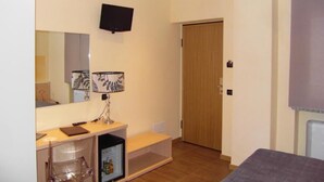 A hotel room with a bed, a desk with a lamp, a TV mounted on the wall, and a door. - Ristorante Locanda Milano (Gambolo)