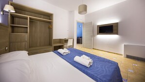 A hotel room with a bed, a desk, a wardrobe, and a TV mounted on the wall.