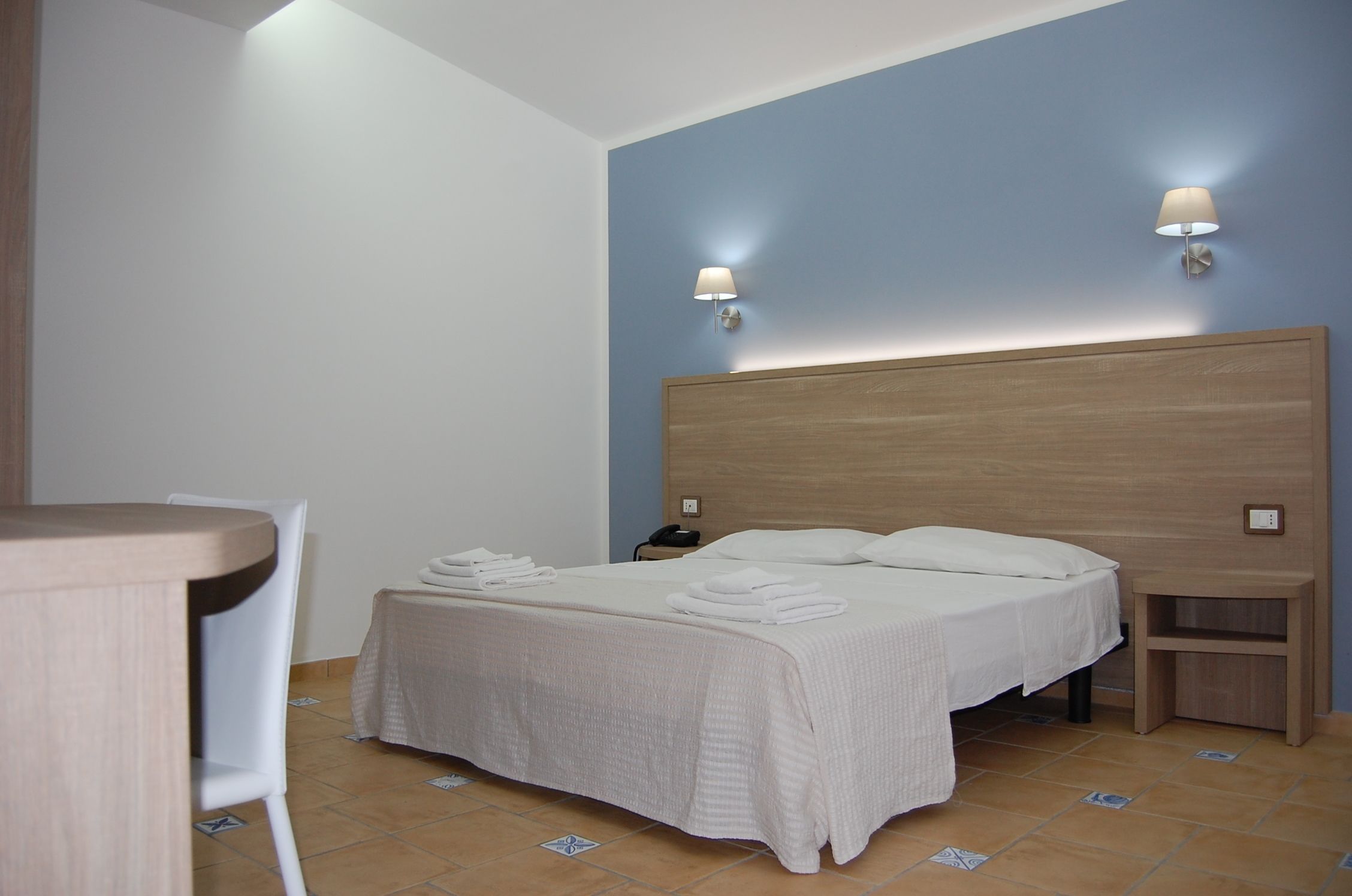 A hotel room with a bed, bedside tables, a desk, and a chair.