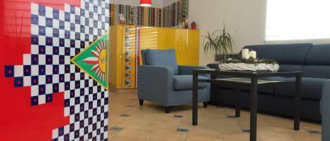 Una sala de estar con un sofá azul, un sillón azul, una mesa de centro y una pared colorida con diseño a cuadros.