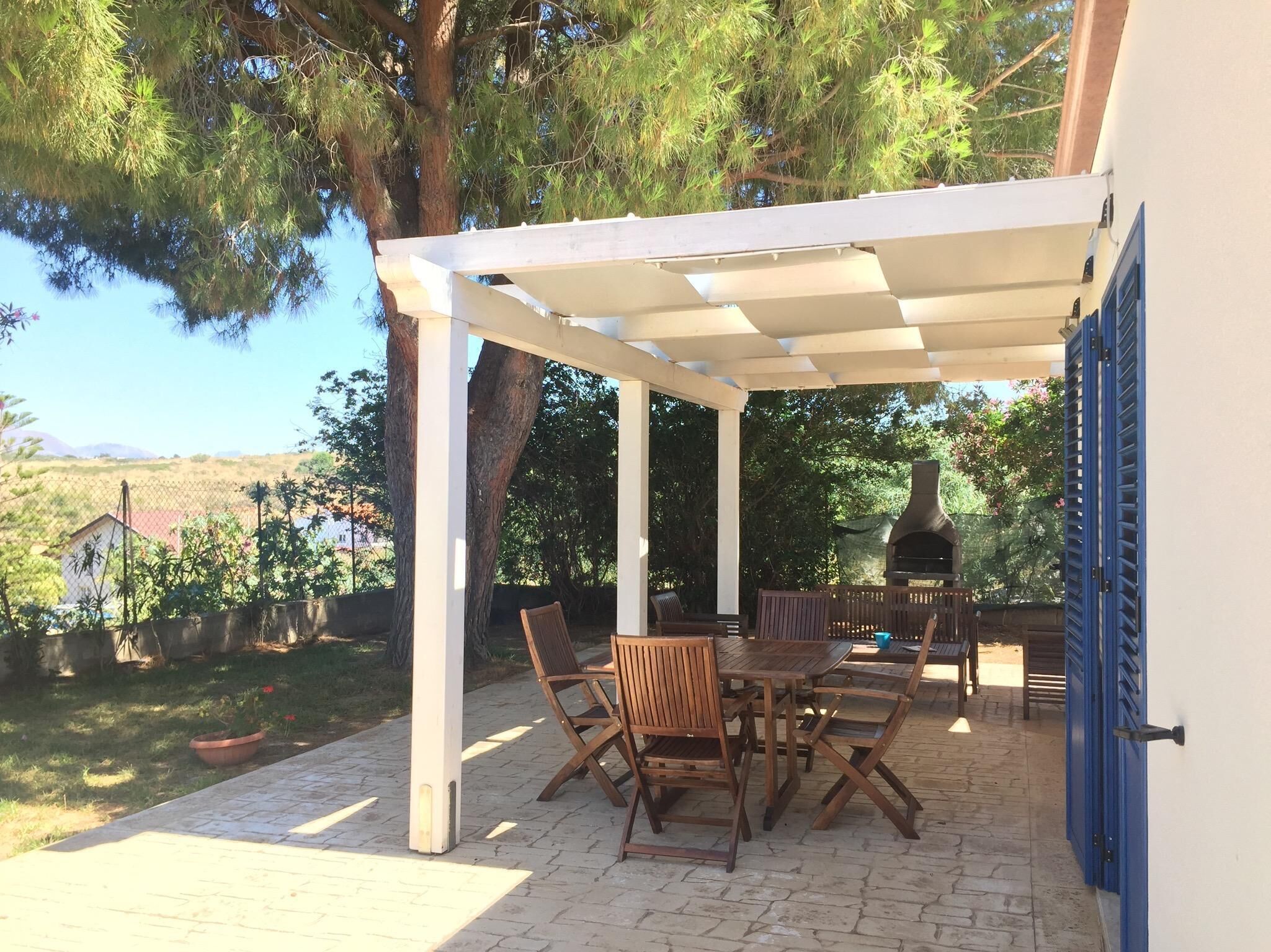 A covered patio with a table and chairs, a grill, and a view of the surrounding landscape.