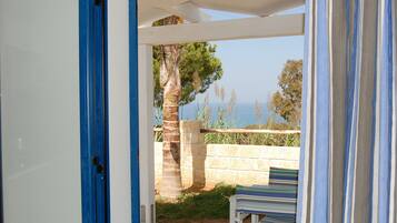 Una puerta abierta que da a un patio con vista al mar, una palmera y un banco a rayas.