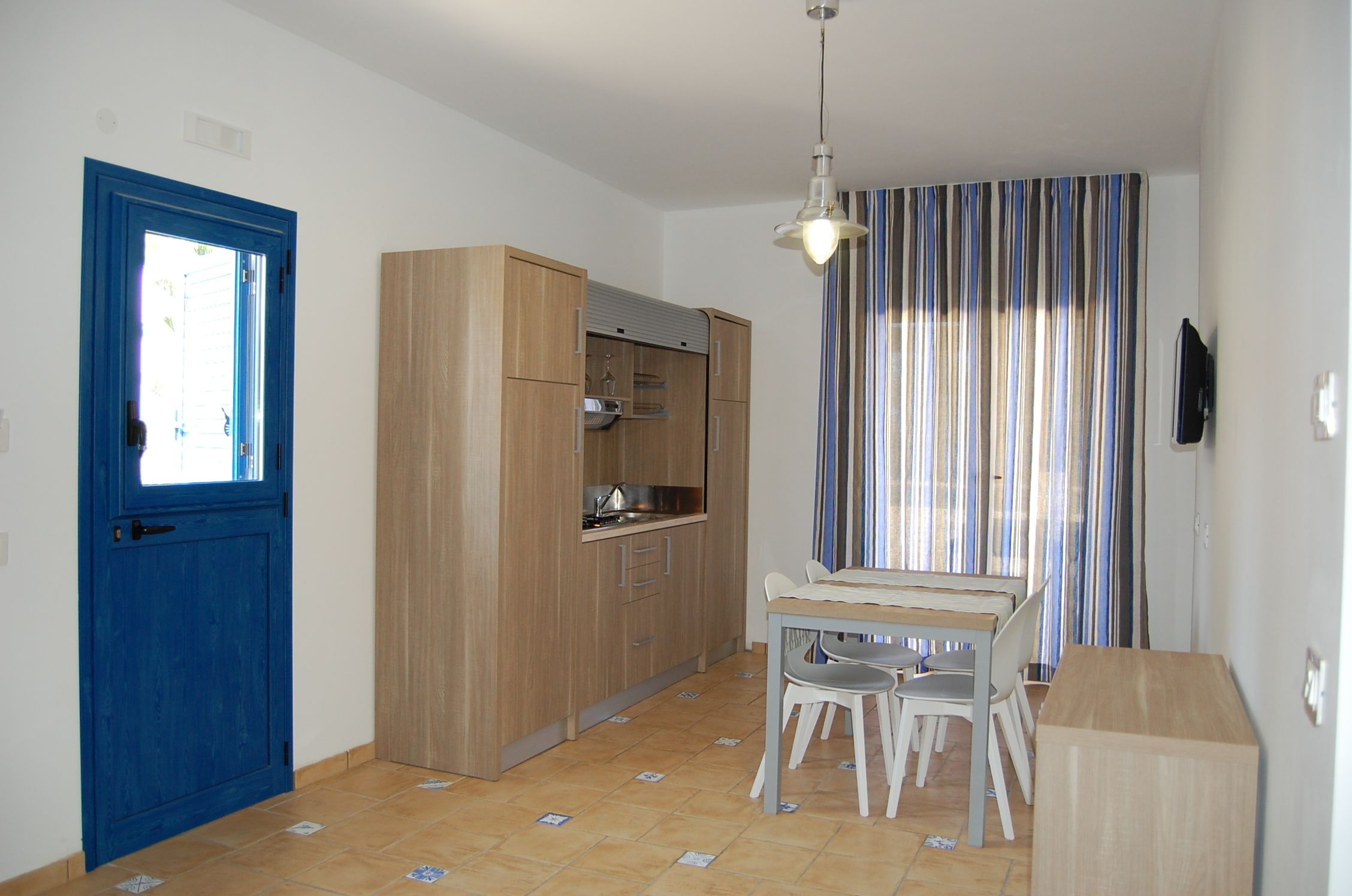 A compact kitchen with wooden cabinets, a dining table with chairs, and a striped curtain.