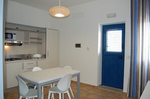 A compact kitchen with a dining area, a blue door, and a hanging light fixture. - Petruso Resort (Balestrate)