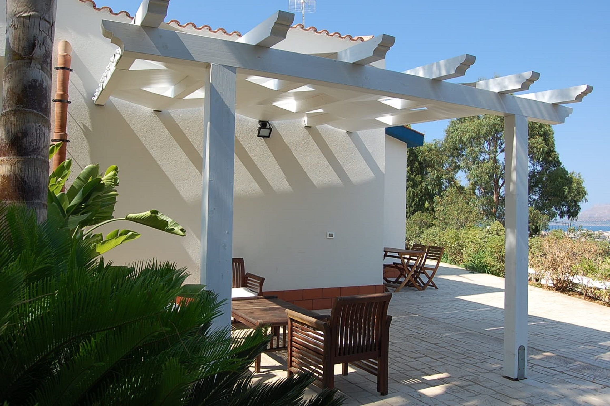 Un espacio de estar al aire libre cubierto con mesas y sillas, una pérgola y vista al mar.