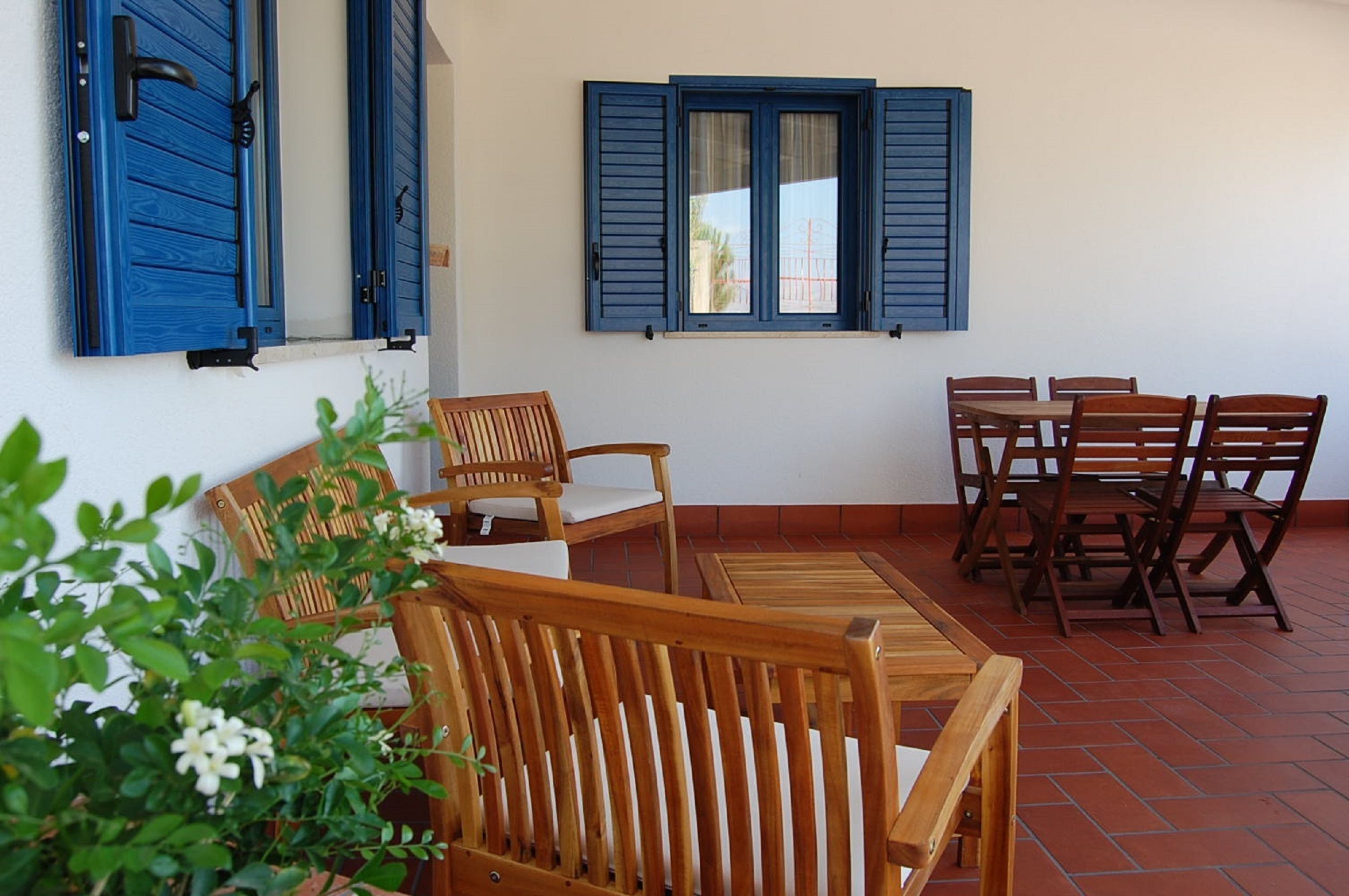 Une terrasse dotée de meubles en bois, notamment des chaises et une table, et une fenêtre avec des volets bleus.