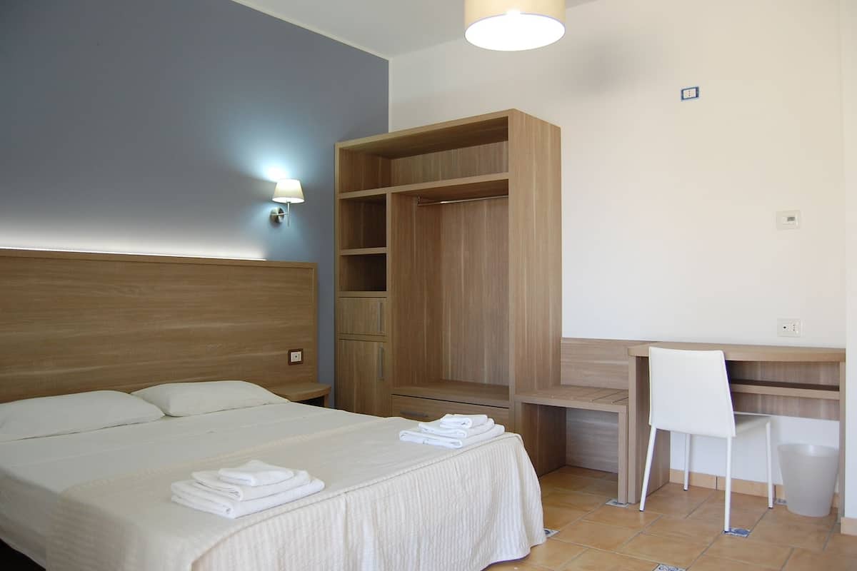 A bedroom with a bed, a wooden wardrobe, a desk, and a chair.