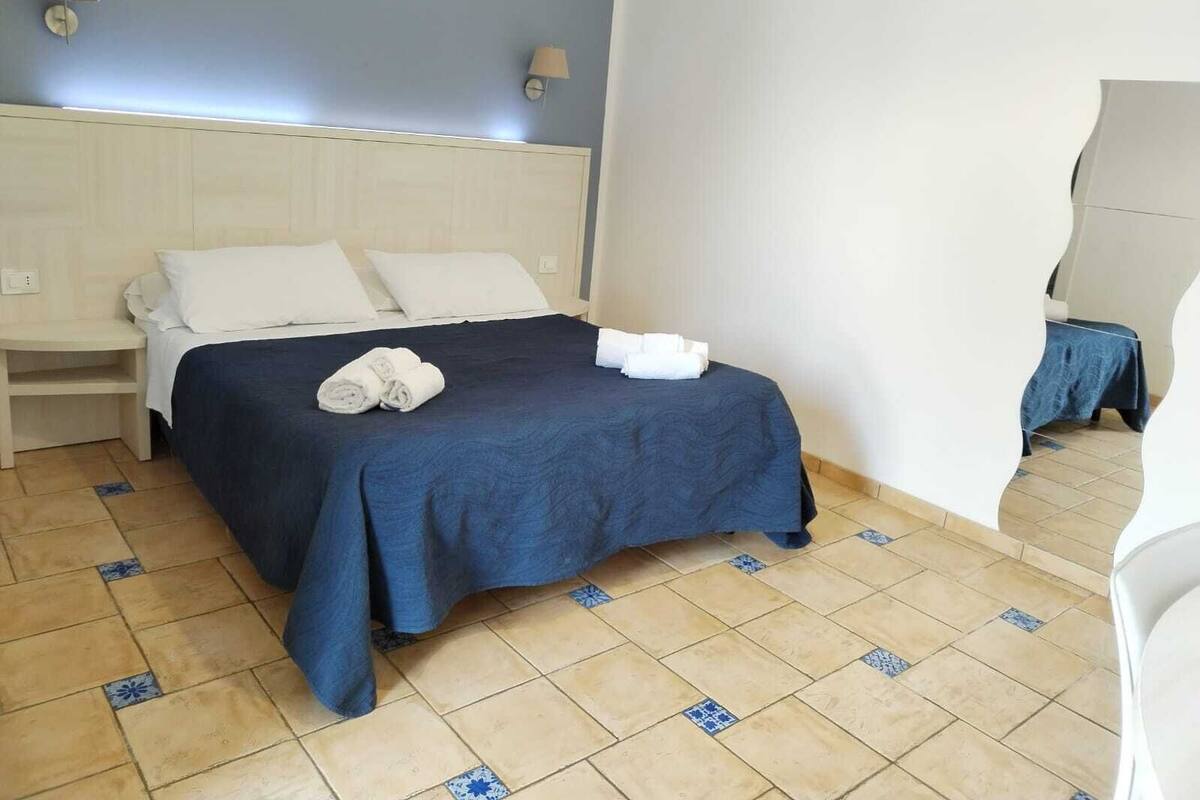 A hotel room with a bed, two bedside lamps, a nightstand, and a blue-patterned floor.