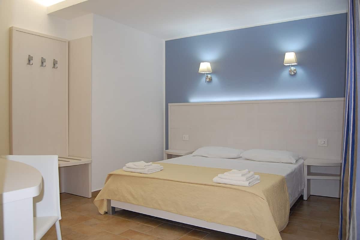 A bedroom with a bed, two bedside lamps, a bedside table, a chair, and a wardrobe.