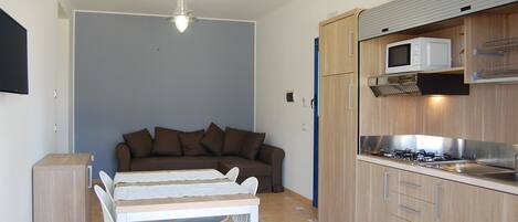 A compact kitchen with a microwave, stove, and wooden cabinets. There is a dining area with a table and chairs.