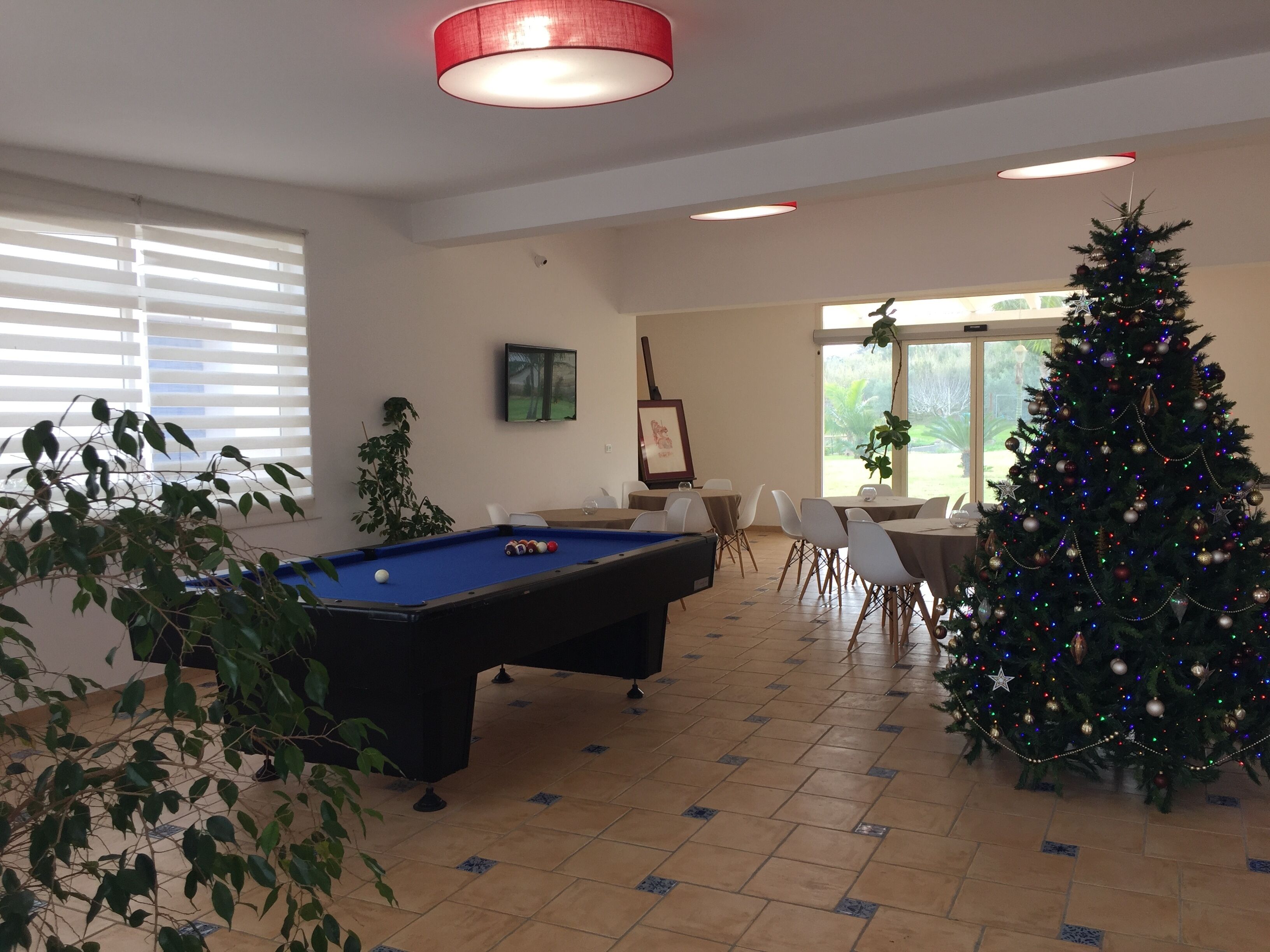 A pool table in a room with a Christmas tree, chairs, and a TV on the wall.