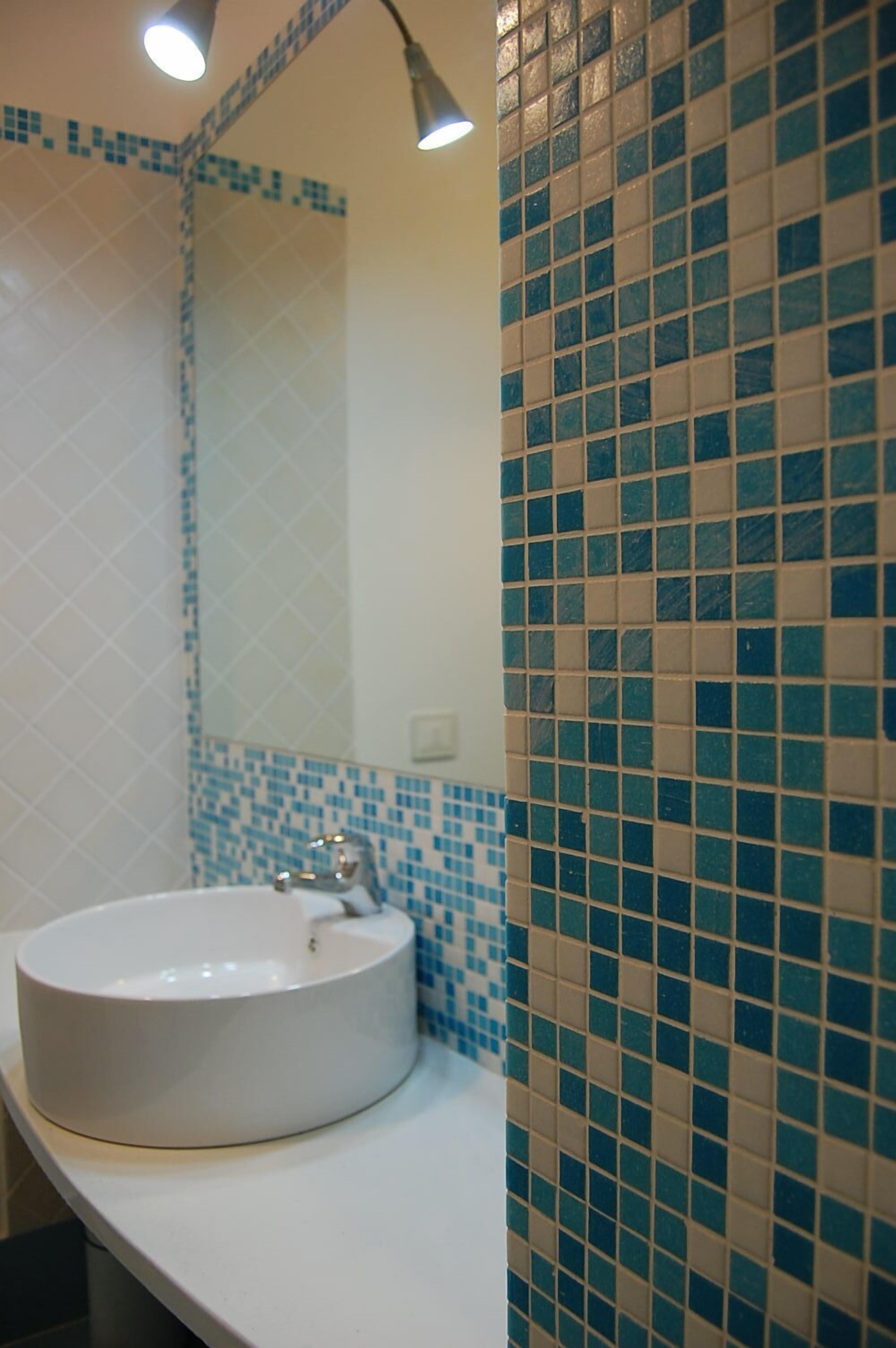 A bathroom with a white sink, blue and beige mosaic tiles, and a mirror.