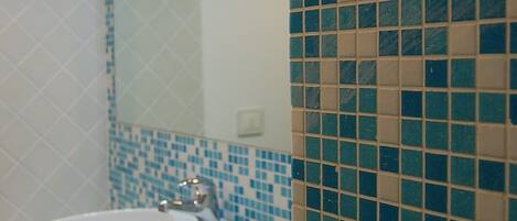 A bathroom with a white sink, blue and beige mosaic tiles, and a mirror.