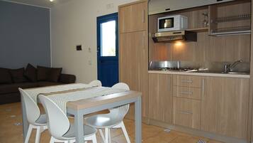 A compact kitchen with wooden cabinets, a microwave, and a sink. There is a dining area with a table and chairs.