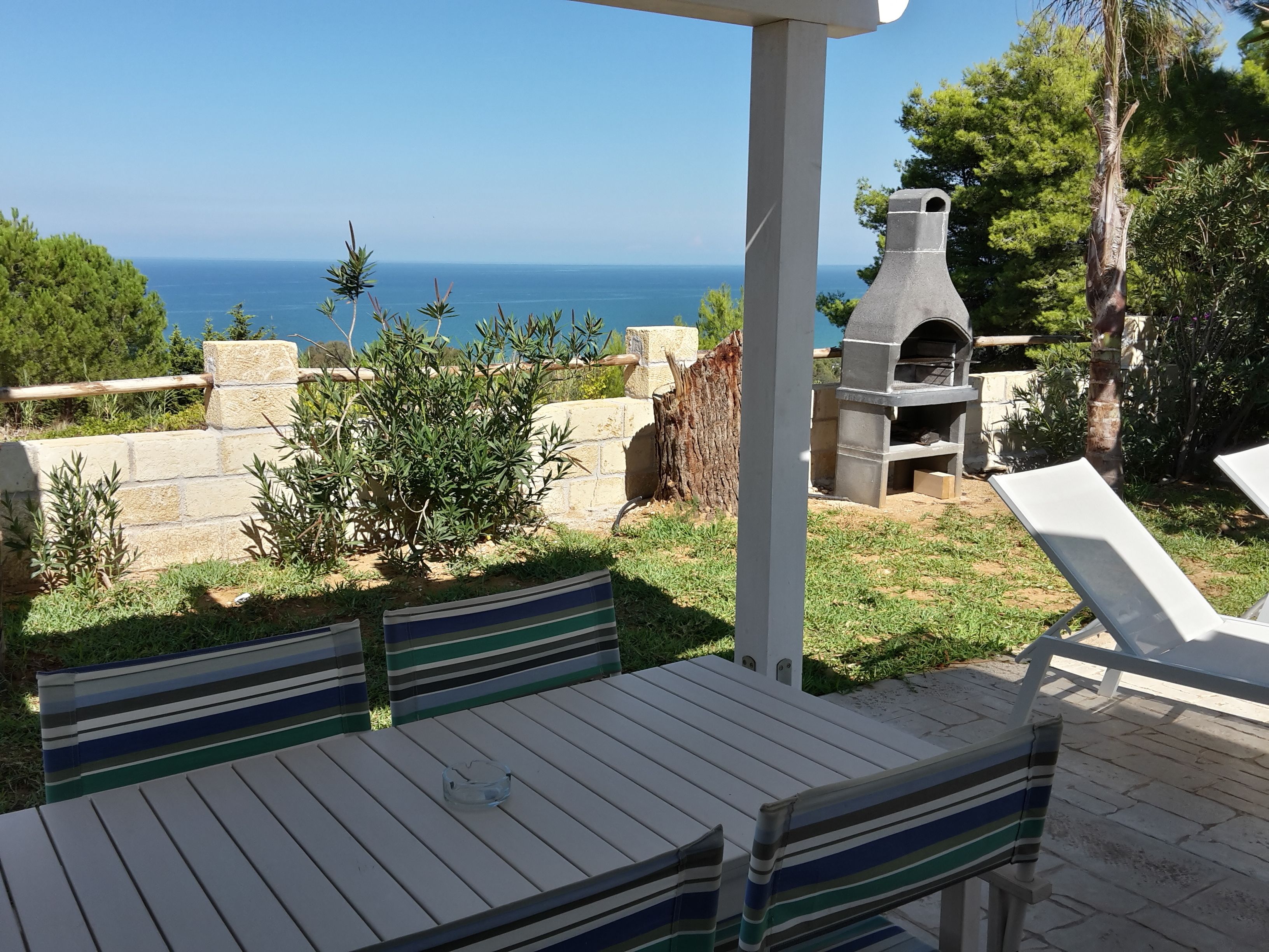 Un patio con tavolo e sedie, un muro in pietra e vista sul mare.