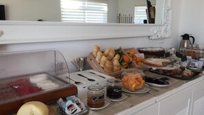 A breakfast buffet with various food items, including bread, pastries, fruits, and condiments.