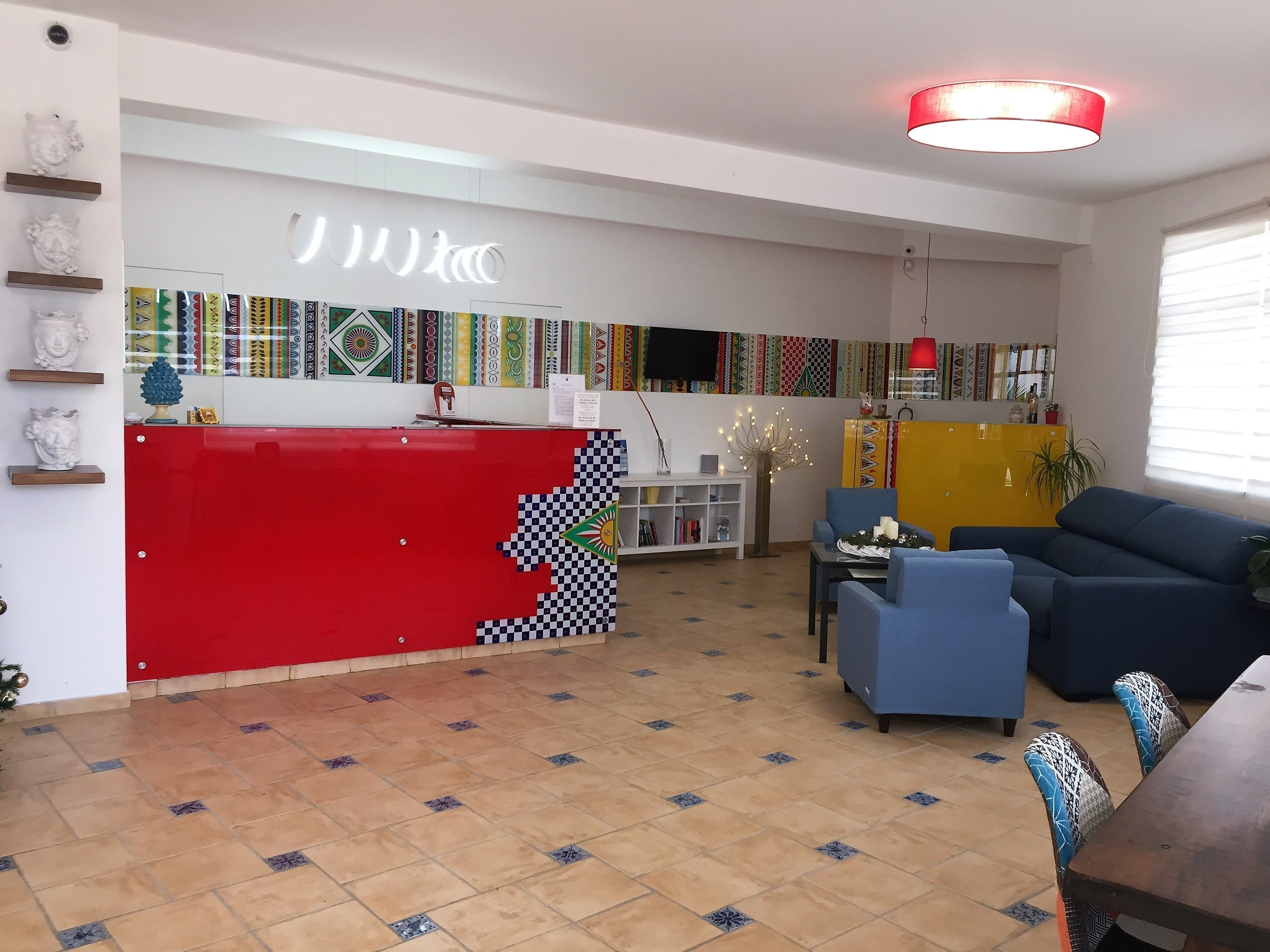 A modern living room with a red and black checkered wall, a blue sofa, and a dining area with patterned chairs.