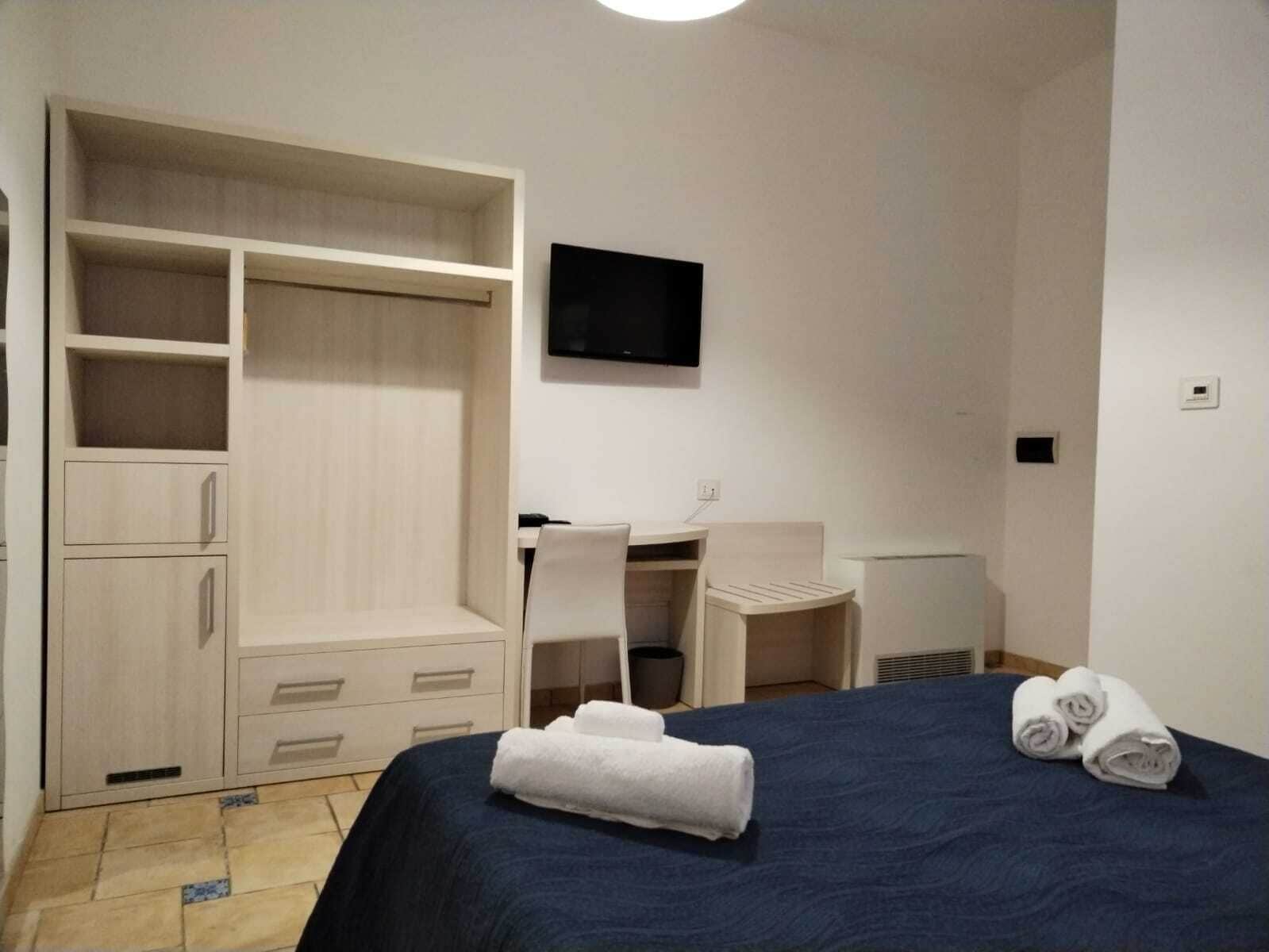 A hotel room with a bed, a desk, a chair, a wardrobe, and a flat-screen TV.