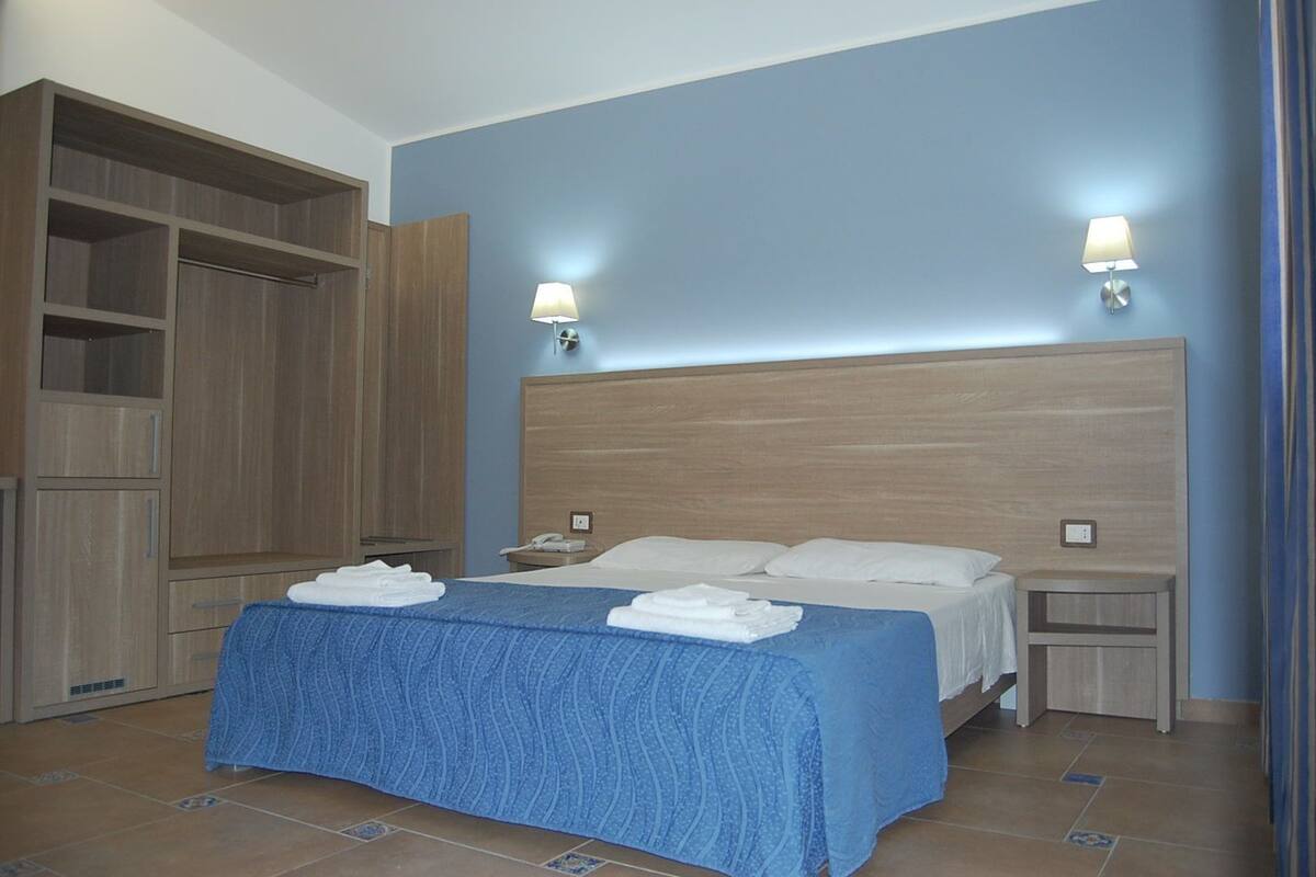 A bedroom with a large bed, two bedside tables, a wardrobe, and a nightstand.