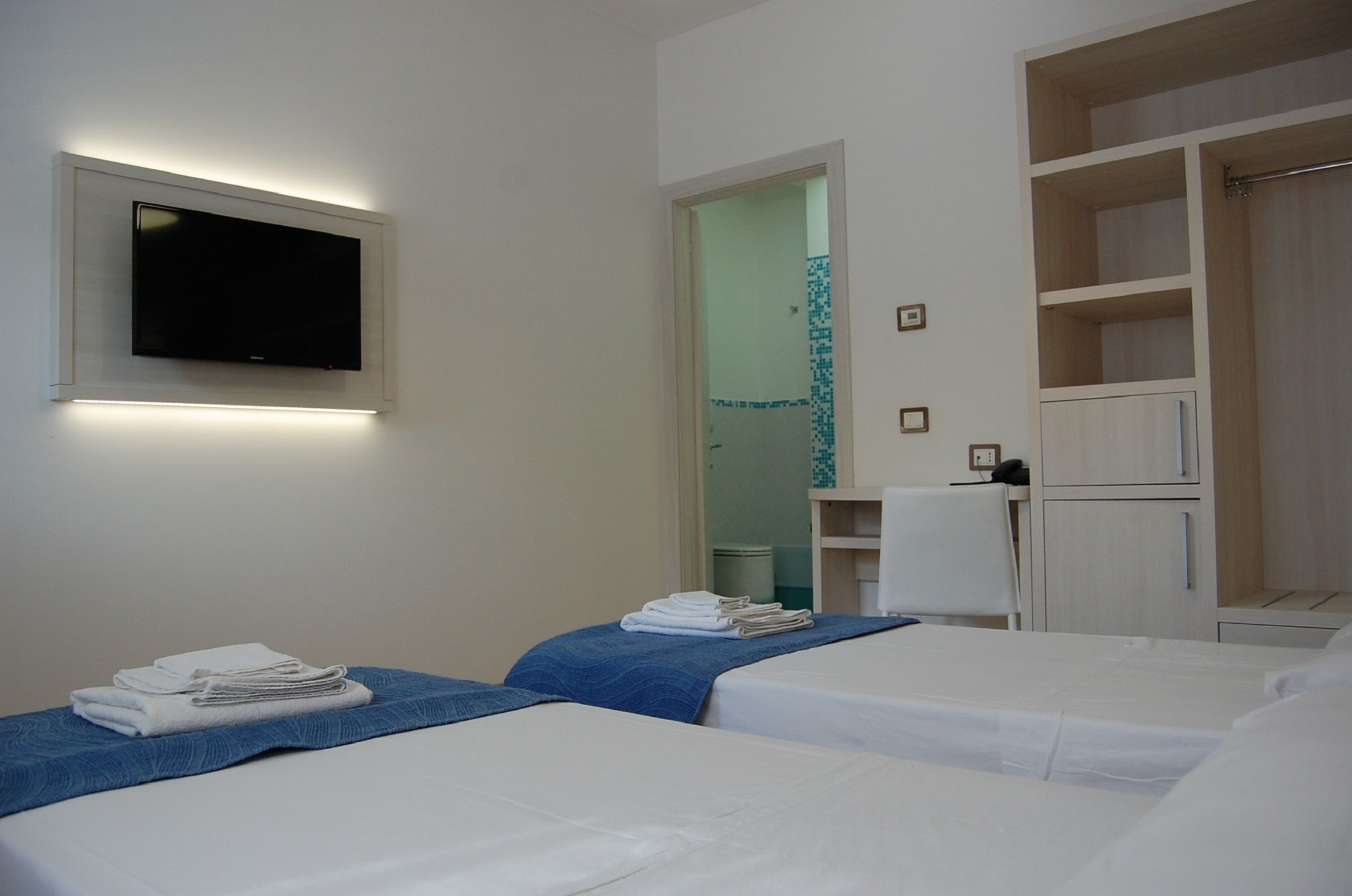 A hotel room with two beds, a TV mounted on the wall, and a wardrobe with open shelves.