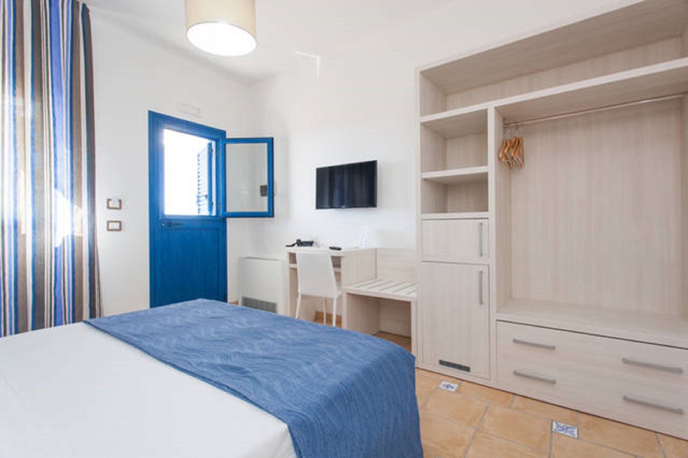 Ein Schlafzimmer mit Bett, Schreibtisch, Stuhl, Kleiderschrank und Fernseher.