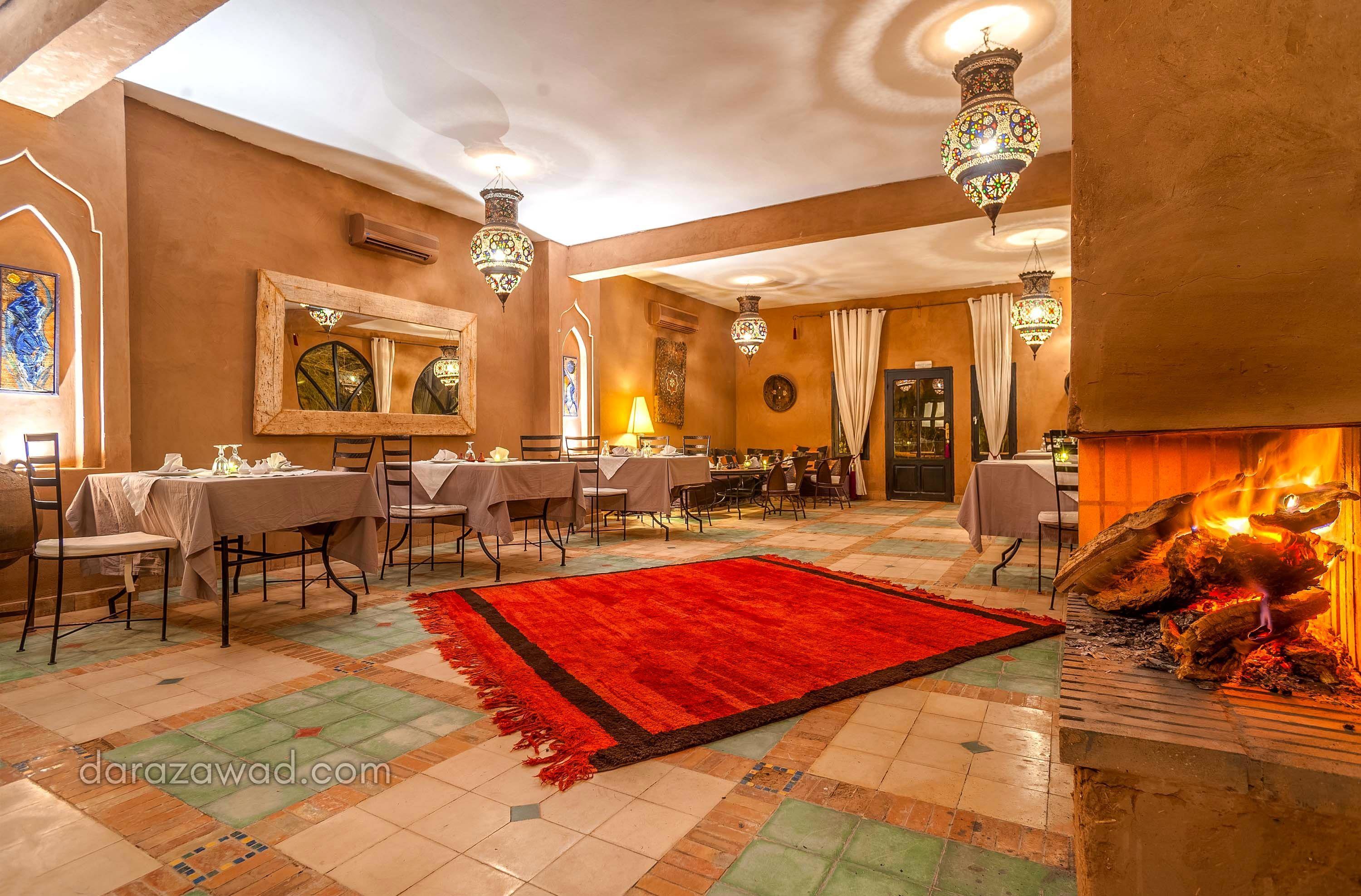 Un espace repas avec des tables dressées pour les invités, une grande moquette rouge et une cheminée où brûle du bois.