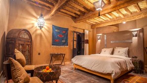 Una habitación tradicional con una cama, una silla, una mesita con fruta y un adorno en la pared.