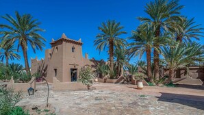 Un edificio tradicional con una torre, rodeado de palmeras y un patio empedrado.