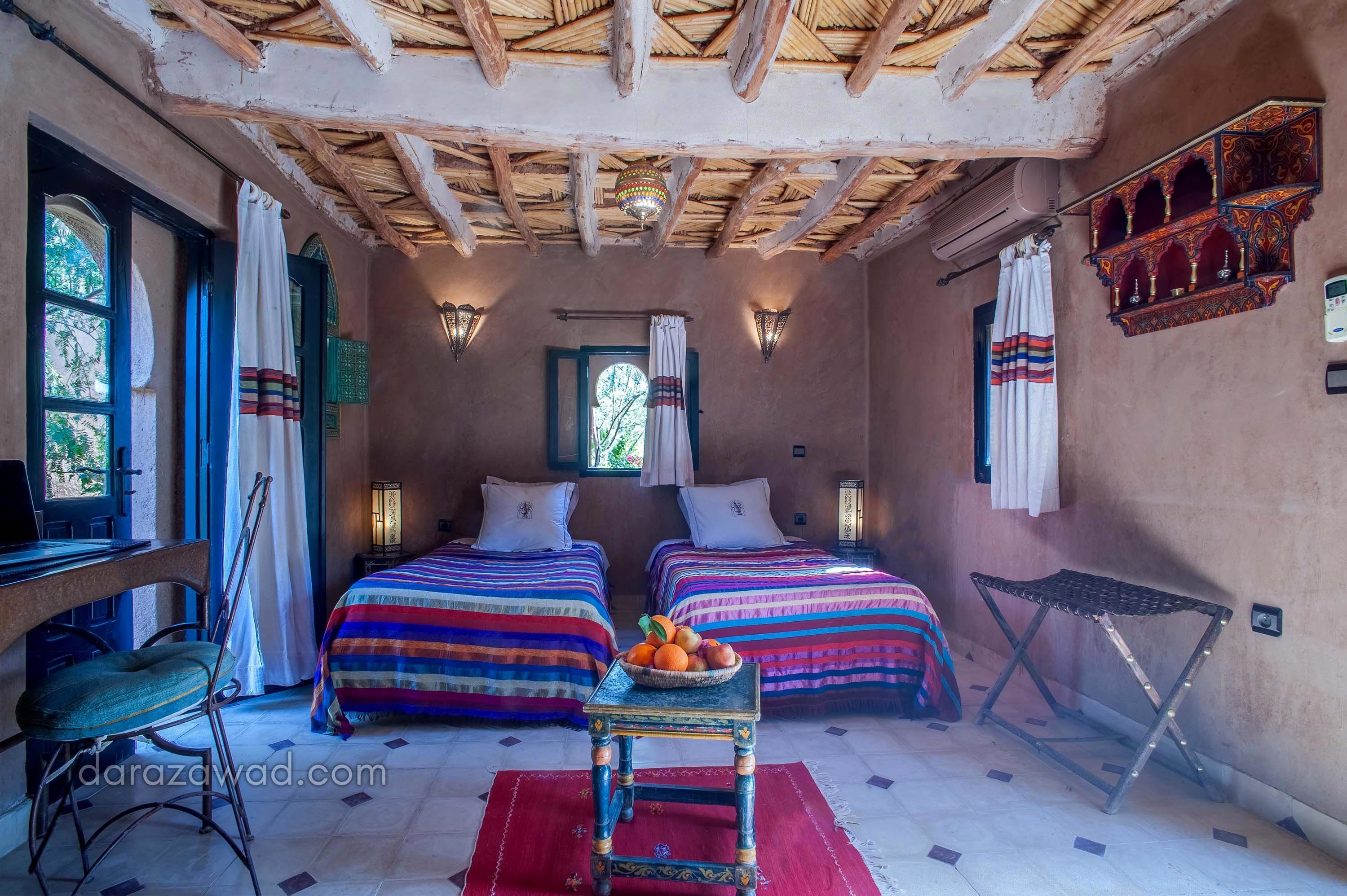 Habitación con dos camas, un escritorio y una silla. Se observa una mesita con fruta y una alfombra roja.
