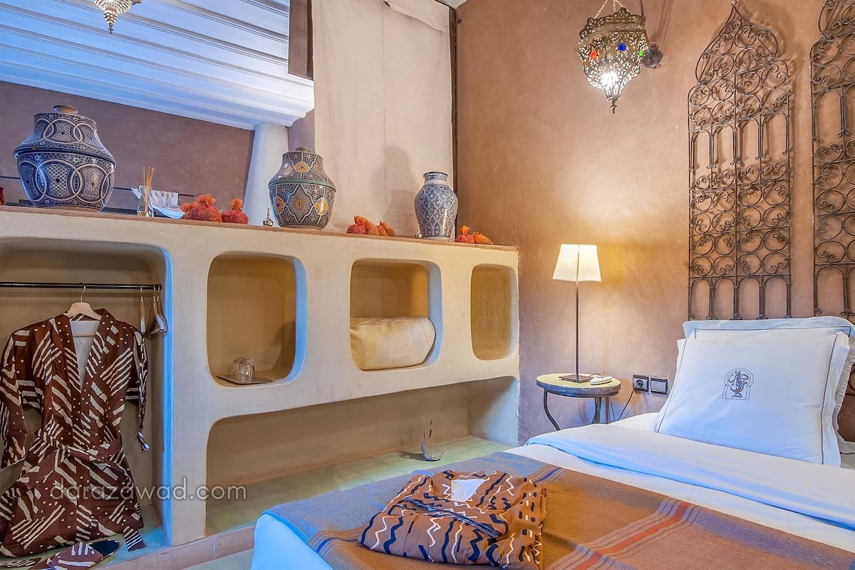 A hotel room with a bed, a vanity with vases, a lamp, and a decorative wall.