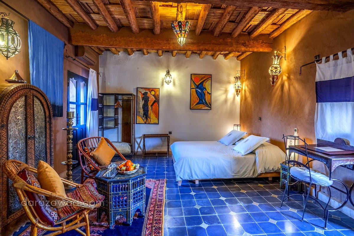 A traditional room with a bed, a desk, and a chair. There are two wall-mounted lamps and a hanging lamp.