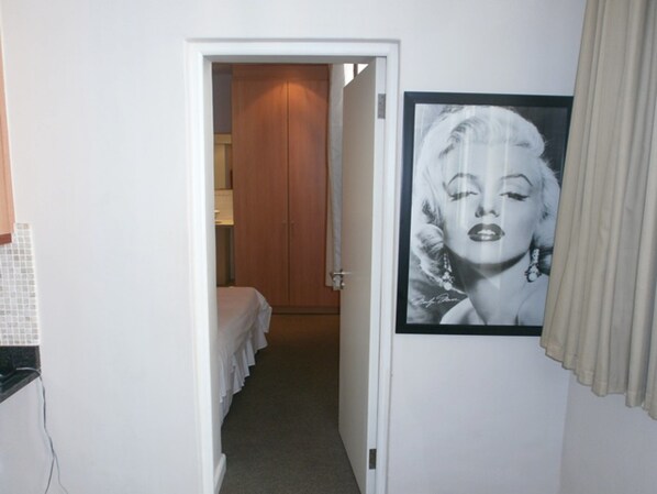 A narrow hallway with a bed at the end, a door leading to a room, and a framed picture on the wall.