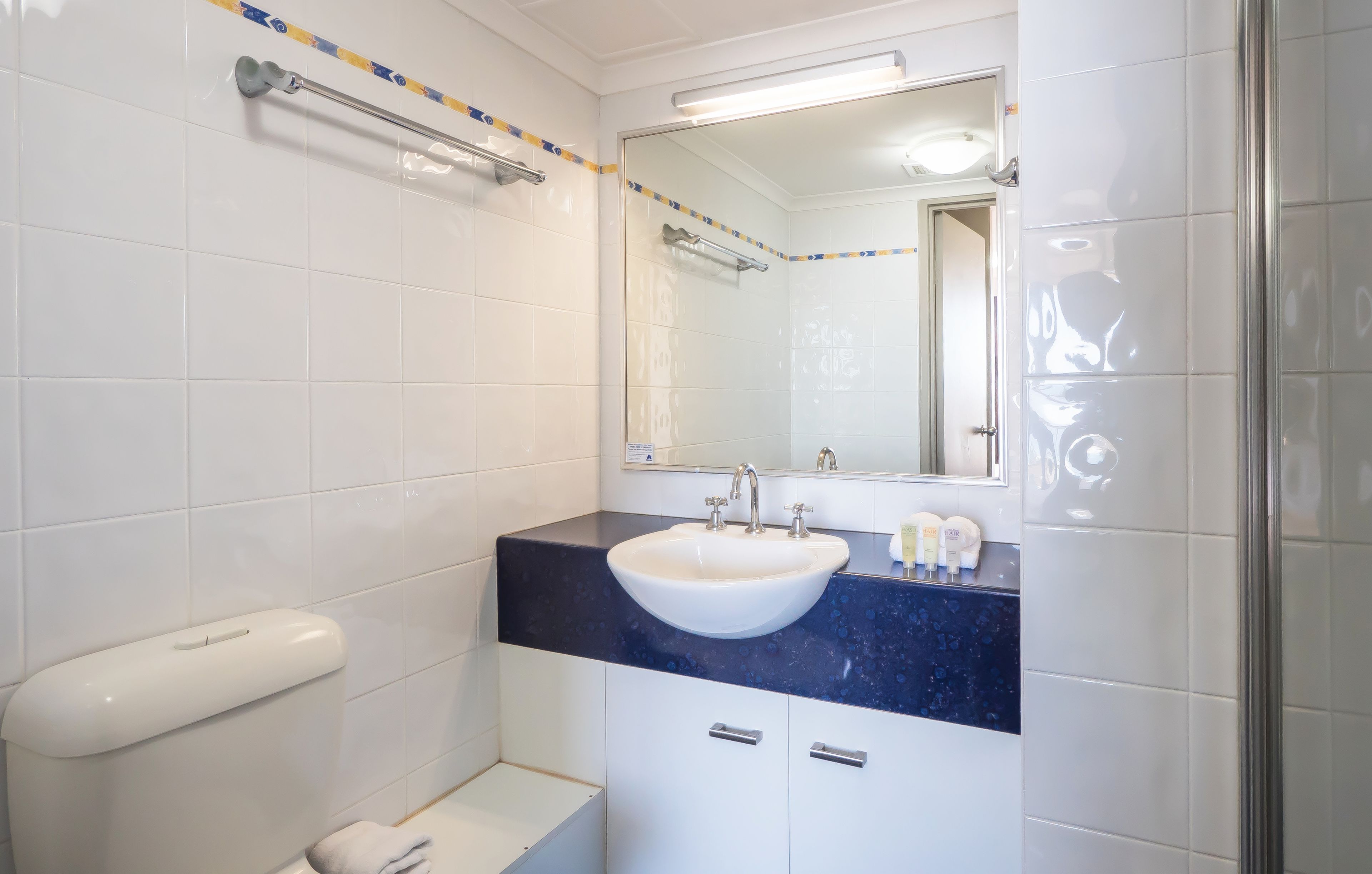 A bathroom with white tiles, a white sink, a mirror, and a towel rack.