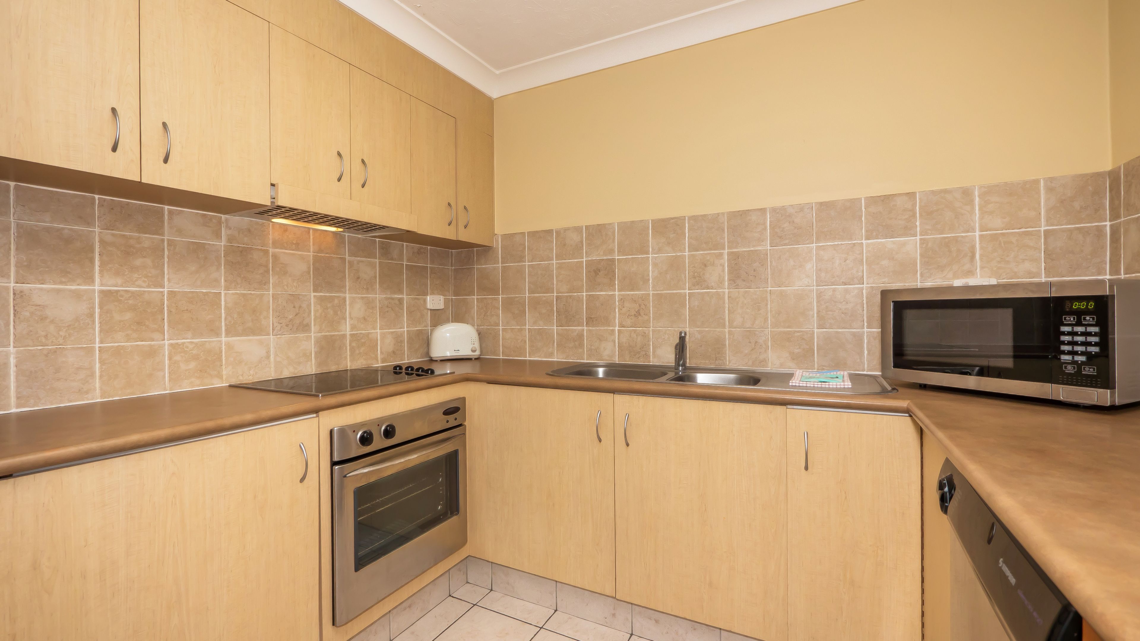 A kitchen with wooden cabinets, a stainless steel oven, a microwave, and a sink.