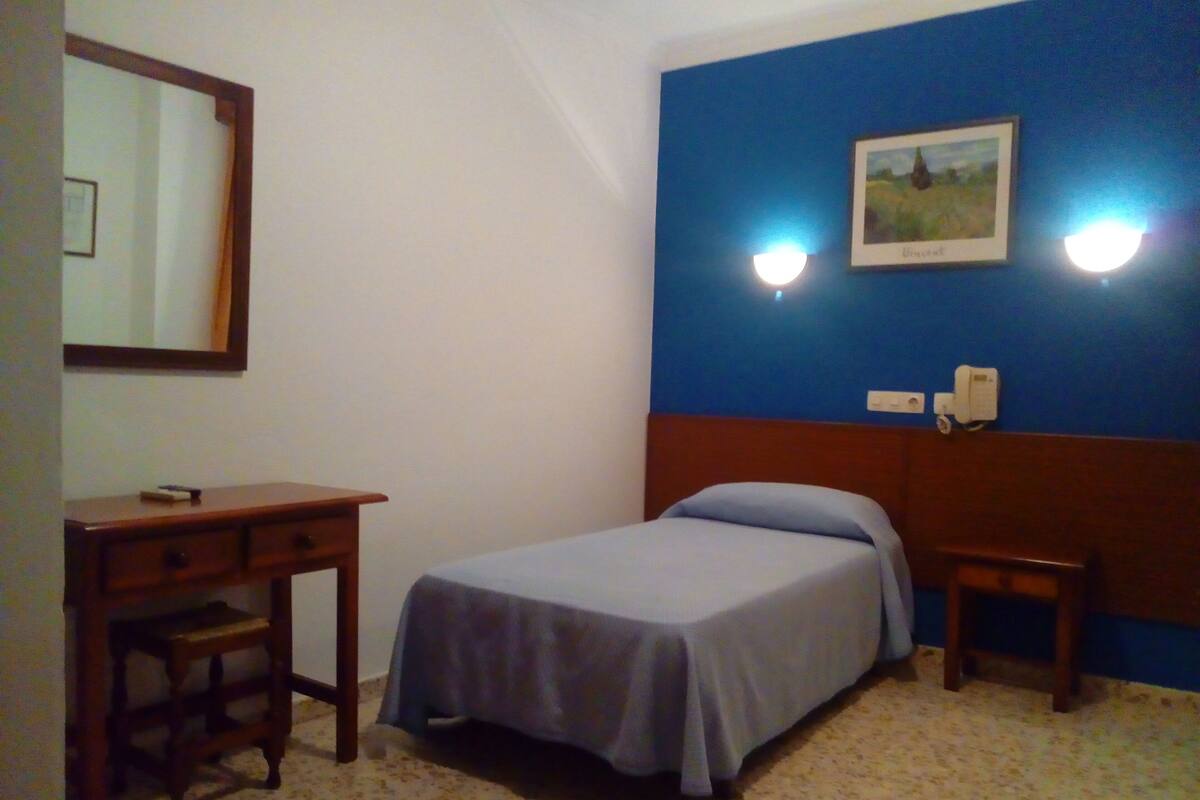 A bedroom with a bed, a nightstand, a dresser, a mirror, and two wall-mounted lights.