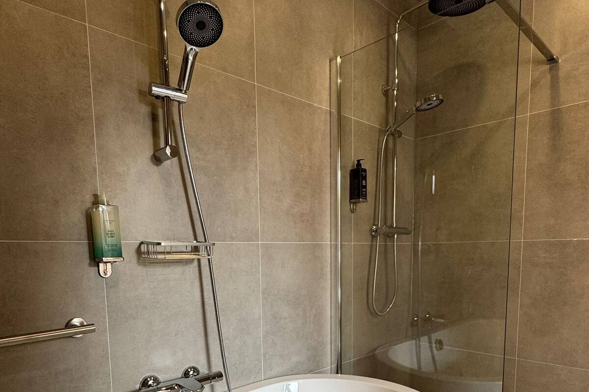 Uma casa de banho moderna com uma banheira independente, uma cabine de chuveiro com vidro e um chuveiro manual.